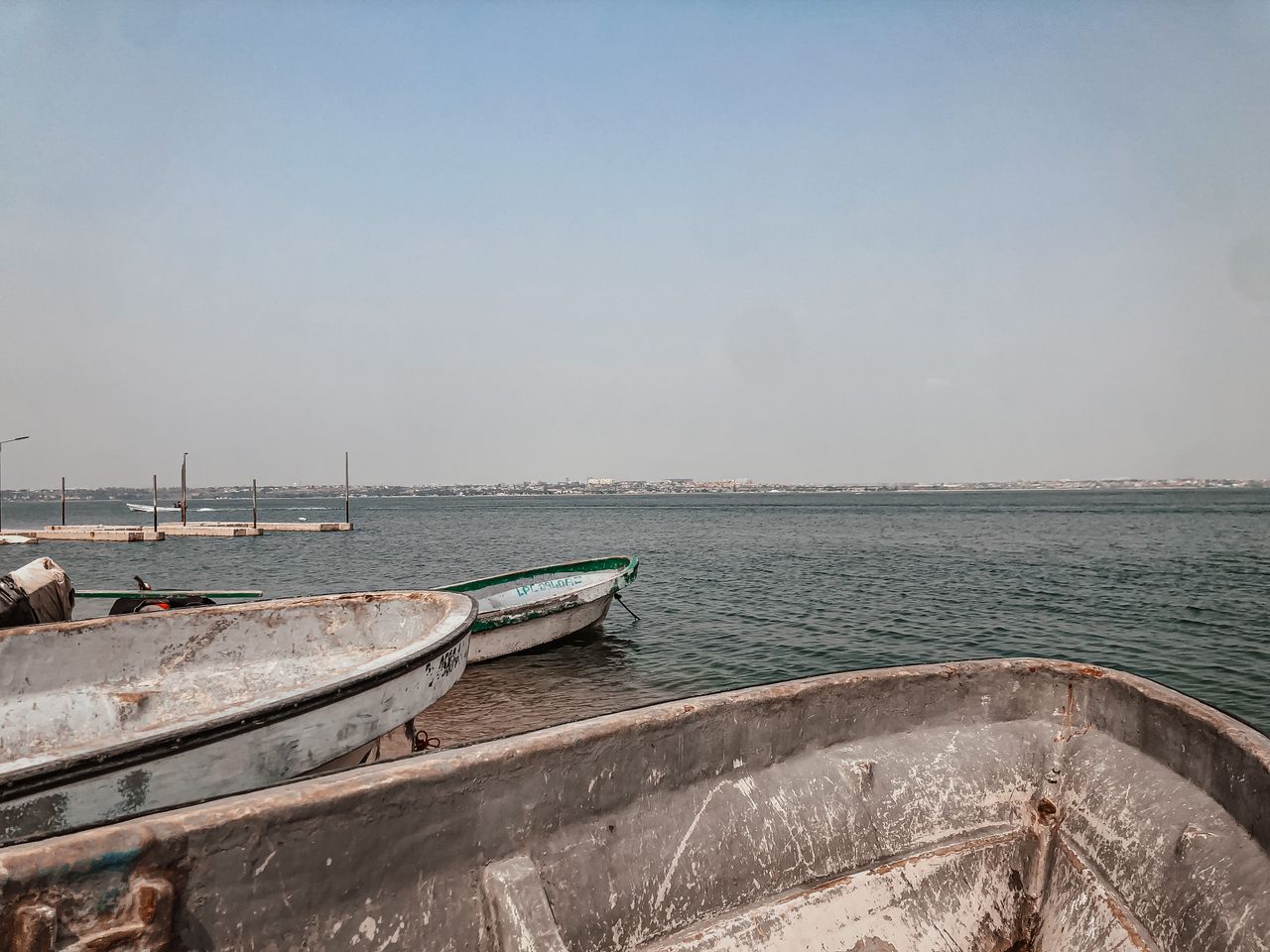 Best eSIM for Angola; a scenic view of calm water under a pale blue sky, with several weathered boats docked at the shore in Angola.