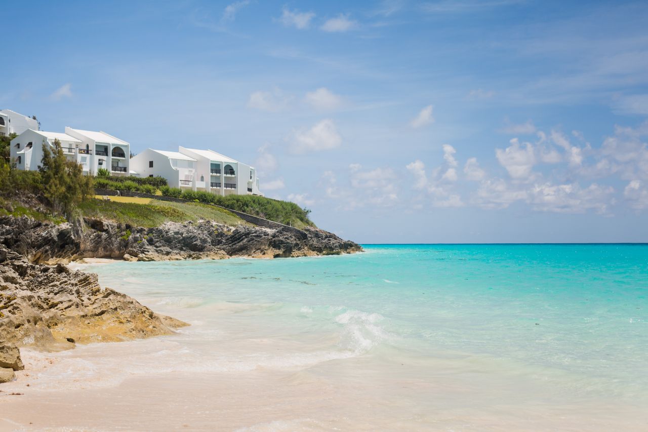Best eSIM for Anguilla; a scenic coastal landscape in Anguilla with white buildings on a rocky cliff overlooking a sandy beach and turquoise ocean.