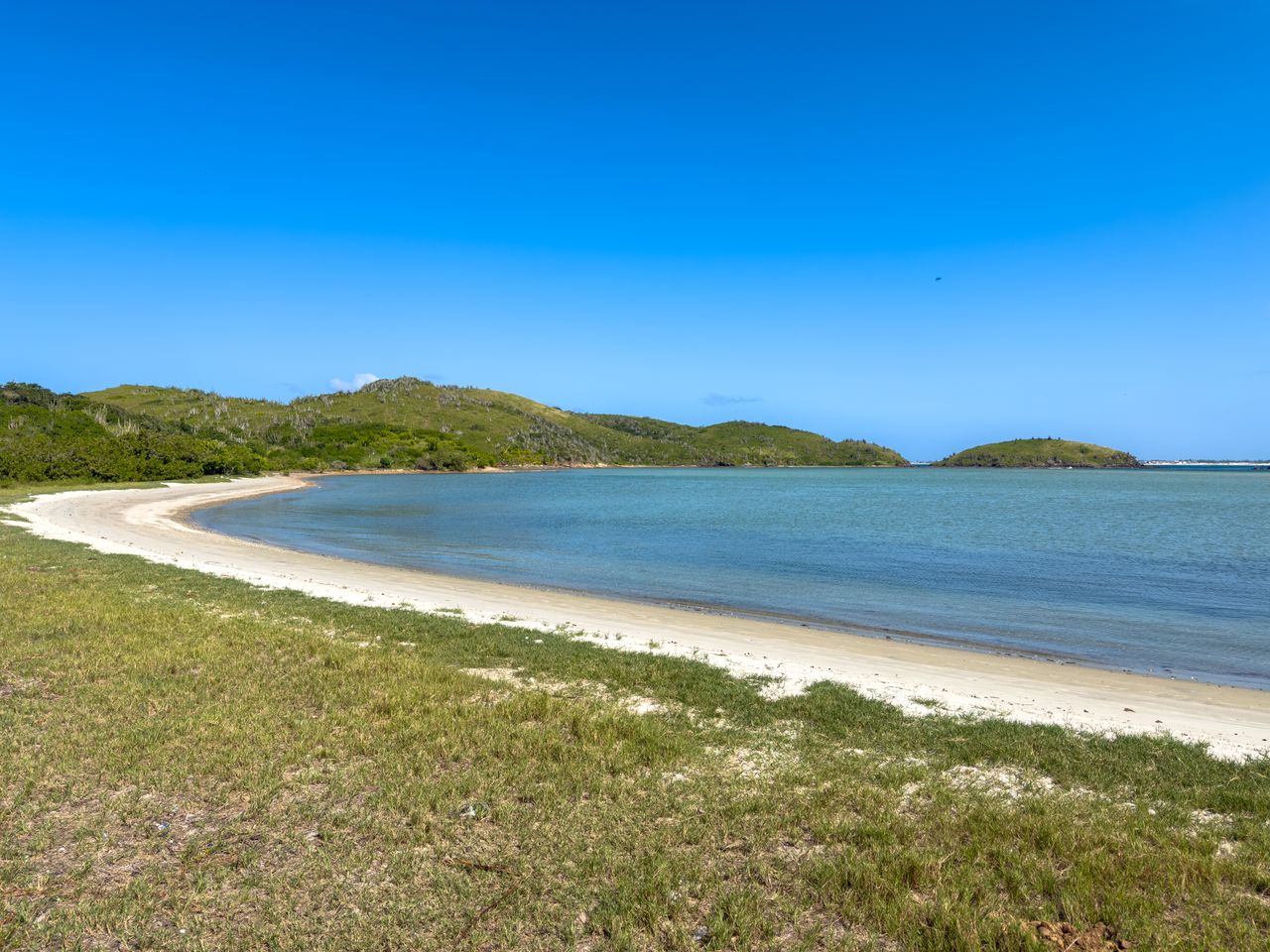 Best Antigua and Barbuda eSIM for travel; a scenic coastal landscape with a sandy beach curving into clear turquoise water in Antigua and Barbuda.