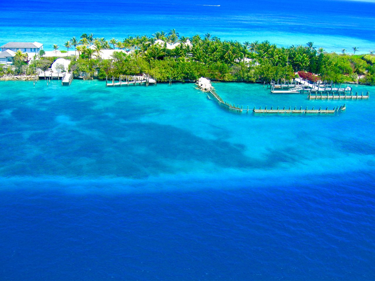 Best eSIM for Bahamas travel; aerial view of a tropical island resort in the Bahamas with turquoise and deep blue ocean water, a long pier extending into the water.