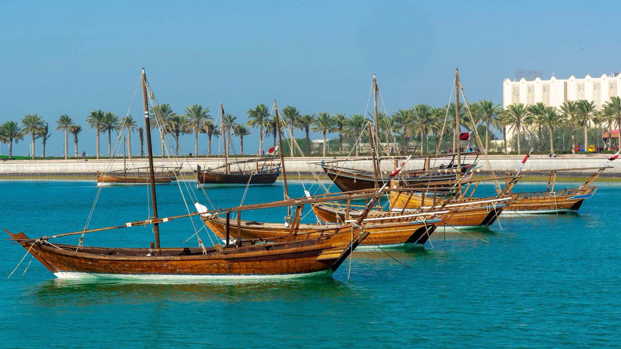 Best eSIM for Bahrain; Dhows in Bahrain moored in a bay with palm trees and white modern building in the background