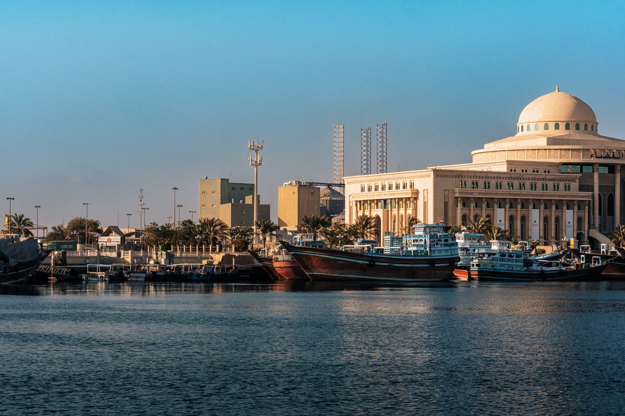 Best Bahrain eSIM for travel; A scenic waterfront view in Bahrain of a large beige domed building beside a harbor, with traditional boats docked.