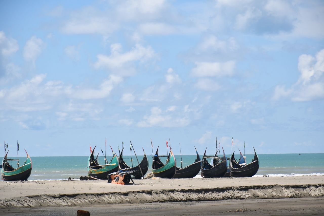 Best Bangladesh eSIM for travel; a beach in Bangladesh with several traditional long boats resting on the sand near the ocean.
