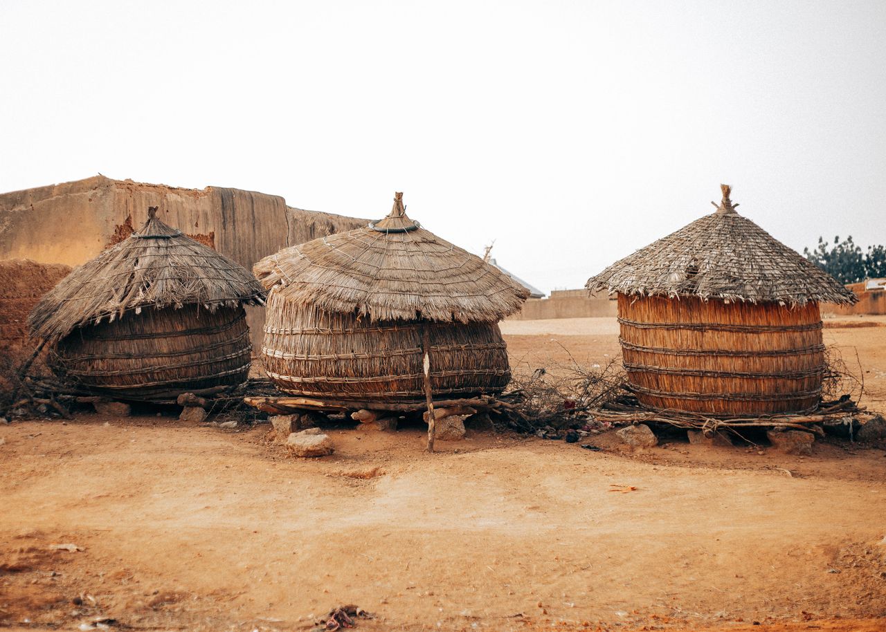 Best eSIM for Benin; three round thatched huts in Benin with conical straw roofs sit on a dry sandy ground under a pale sky, with earthen walls in the background.