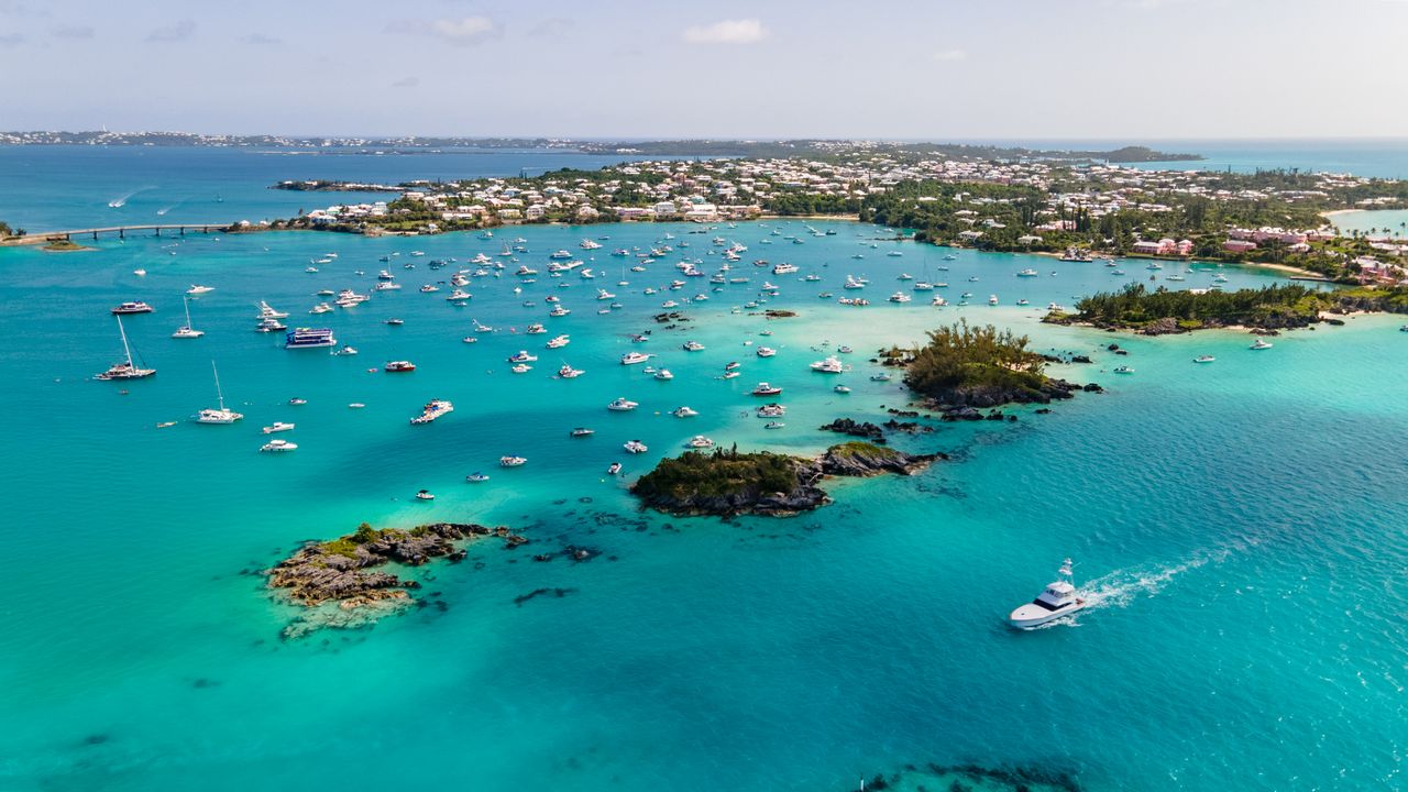 Best Bermuda eSIM for travel; aerial view of a tropical bay in Bermuda with bright turquoise water, numerous anchored boats, rocky islands, and a shoreline lined with white buildings.