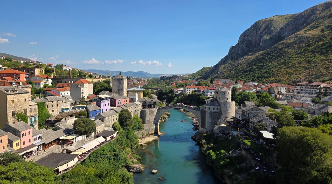 Best eSIM for Bosnia & Herzegovina travel - photo of old mountain village with river running through it and mountains in the background.