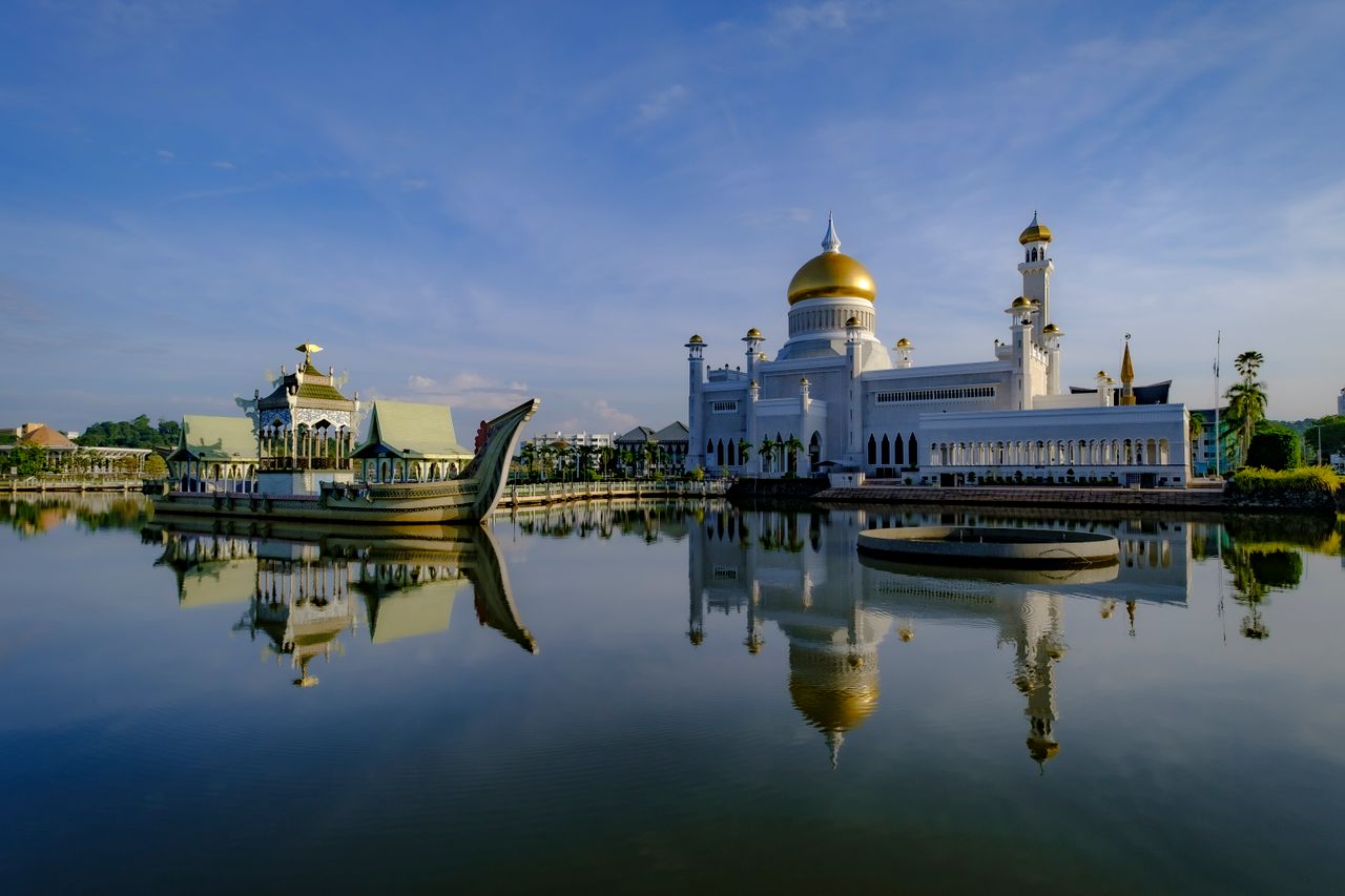 Best eSIM for Brunei Darussalam; a white mosque with golden domes reflected in calm water in Brunei Darussalam.