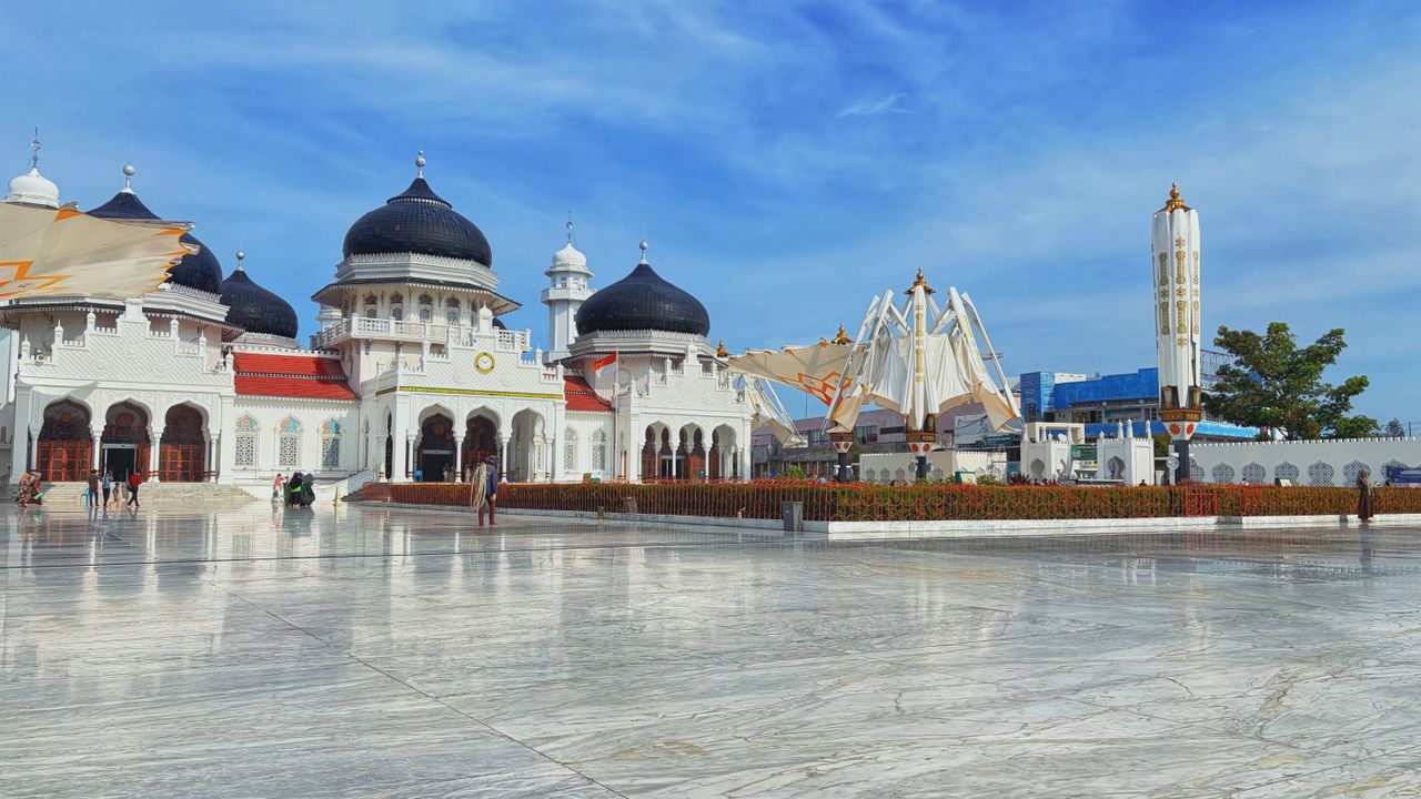 Best Brunei Darussalam eSIM for travel; a large white mosque with multiple dark blue domes, a tall white minaret, and a modern white tower under a bright blue sky in Brunei Darussalam.