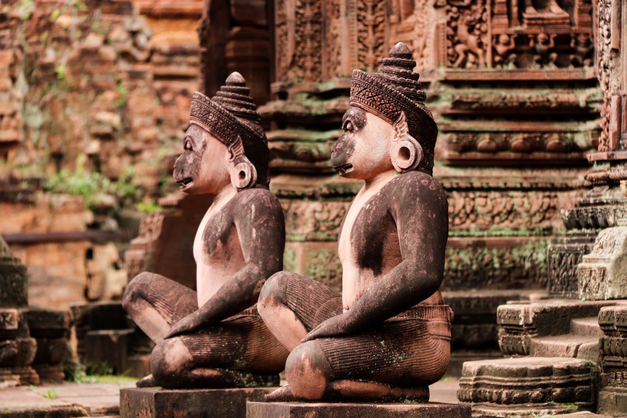 Best Cambodia eSIM for travel; two carved stone statues of seated monkeys with earrings and hats, positioned in front of an ancient temple in Cambodia.