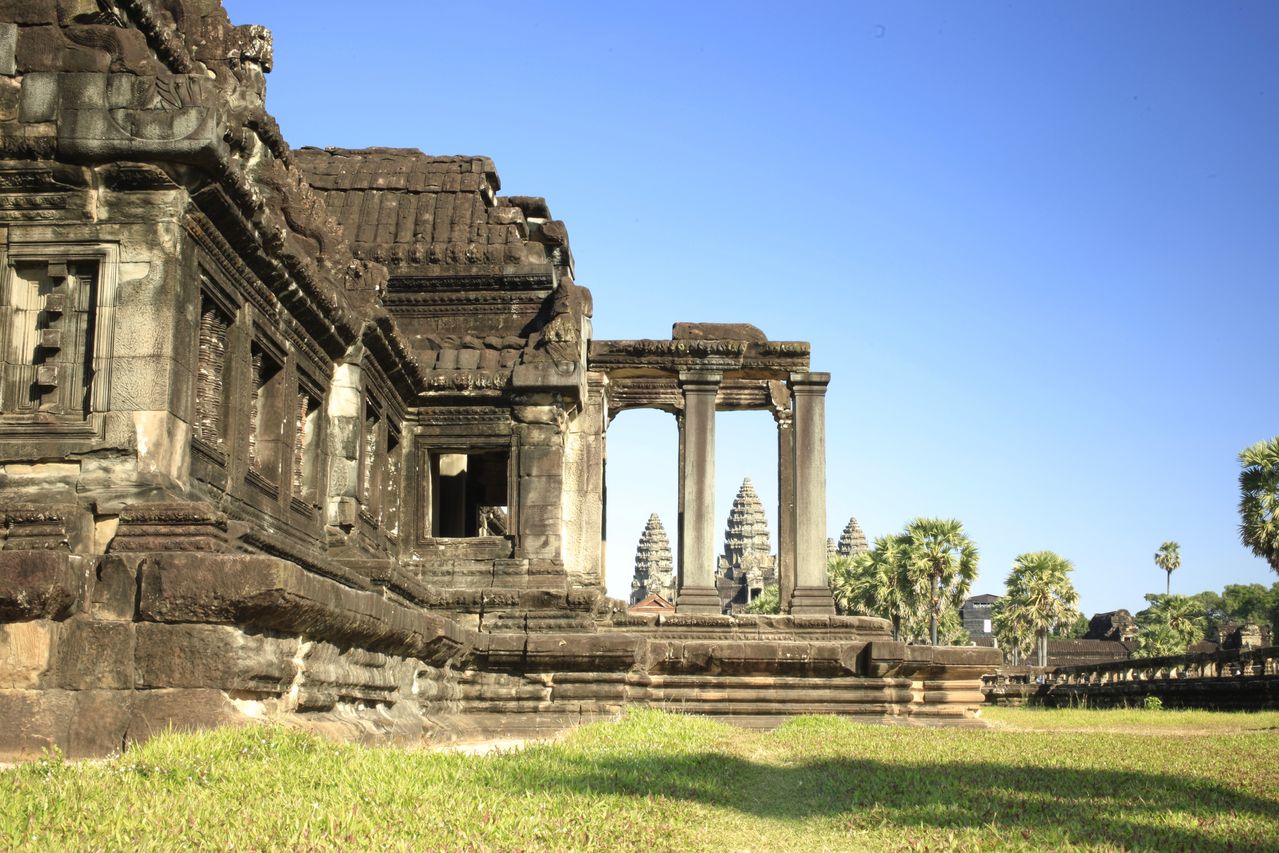 Best eSIM for Cambodia; ancient stone temple ruins in Cambodia, with grass in the foreground and palm trees in the distance.