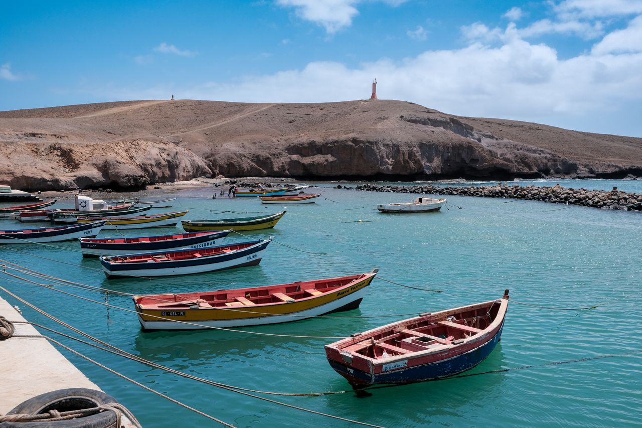 Best eSIM for Cape Verde; a coastal harbor in Cape Verde with several small colorful boats anchored in turquoise water, with rocky brown cliffs.