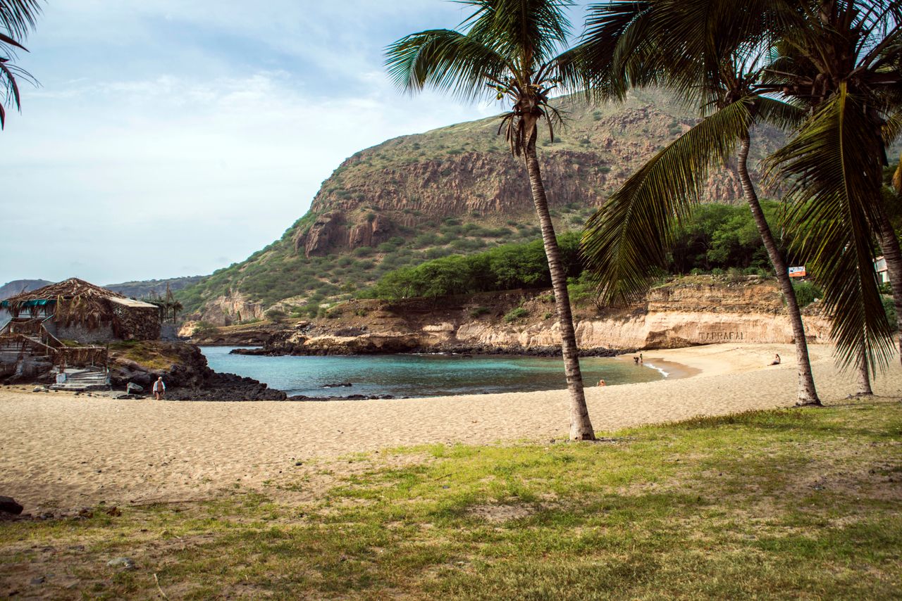 Best Cape Verde eSIM for travel; a beach in Cape Verde with palm trees, a mountain, and a small building.