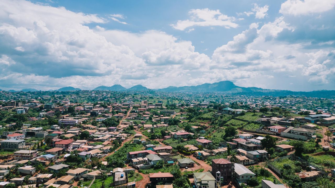 Best Central African Republic eSIM for travel; a densely built town with many houses, roads, and greenery under a bright blue sky with with mountains in the distance.
