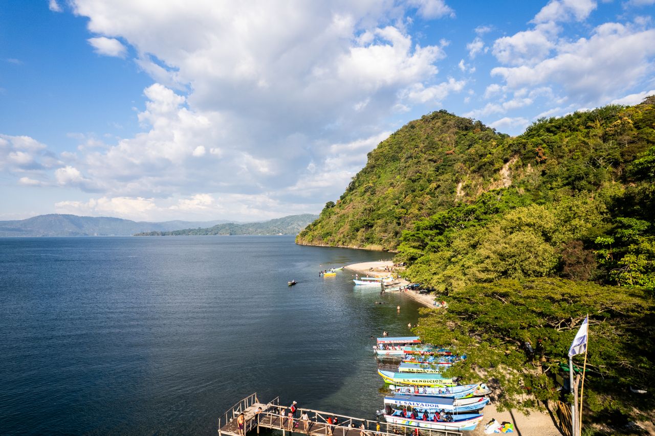 Best eSIM for El Salvador travel; a scenic view of a coastal bay in El Salvador with deep blue water, a steep green hillside, white clouds, and several small boats docked along the shore.