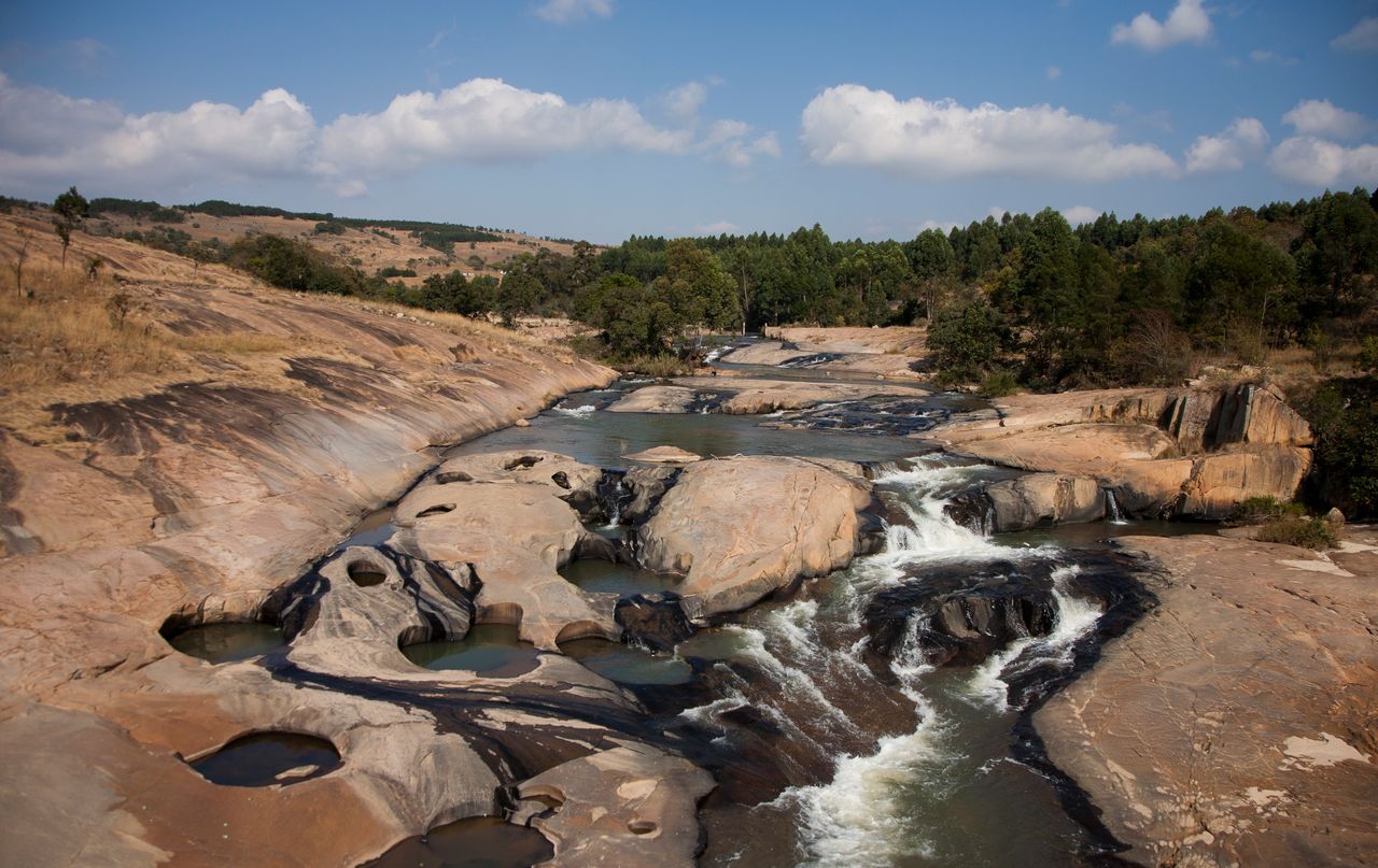 Best Eswatini eSIM for travel; a scenic landscape in Eswatini of a rocky river with cascading waterfalls, surrounded by tan rock formations, and green trees.