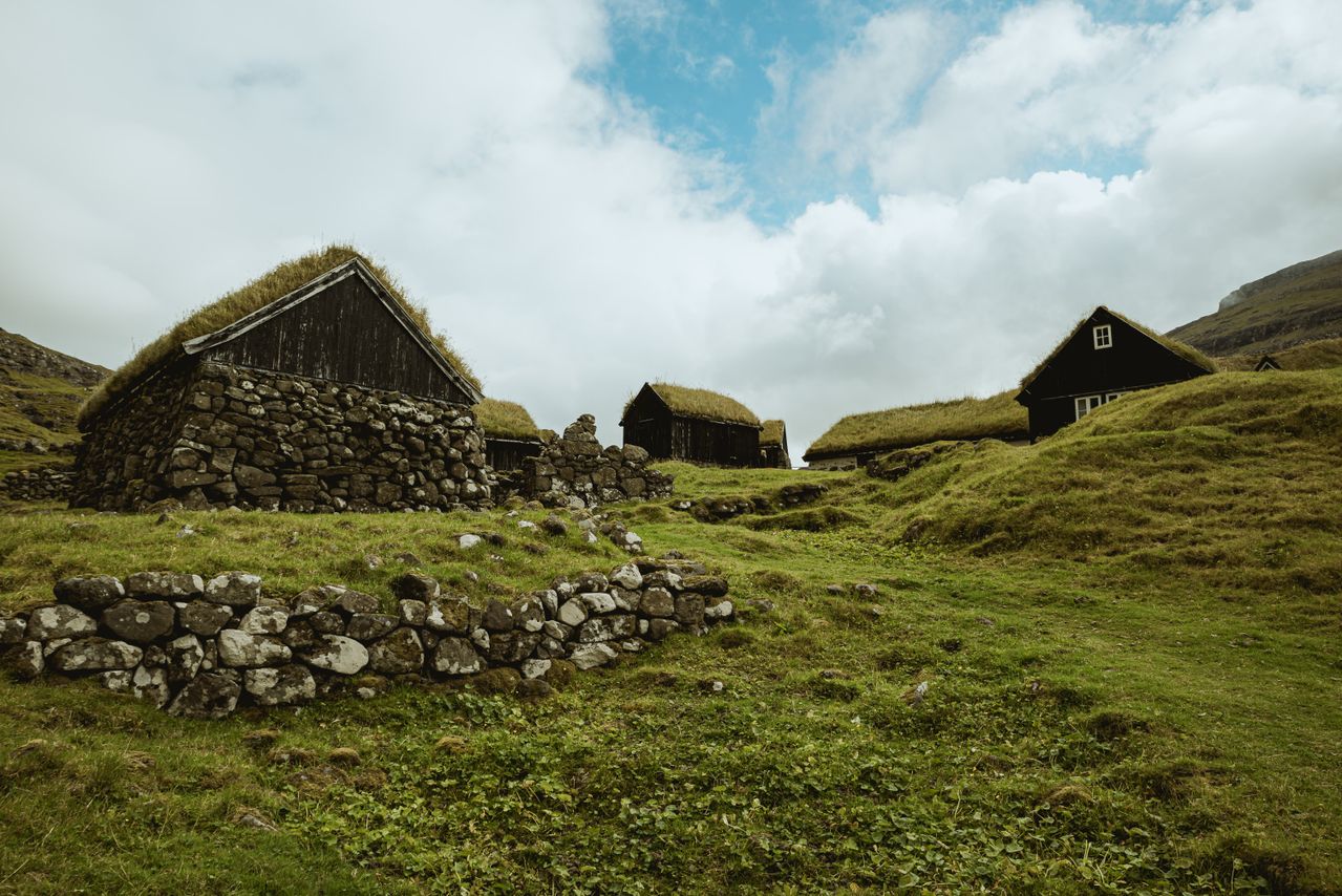 Best eSIM for Faroe Islands; scenic landscape of traditional stone houses on Faroe Islands, with grass-covered roofs nestled on a green hillside.