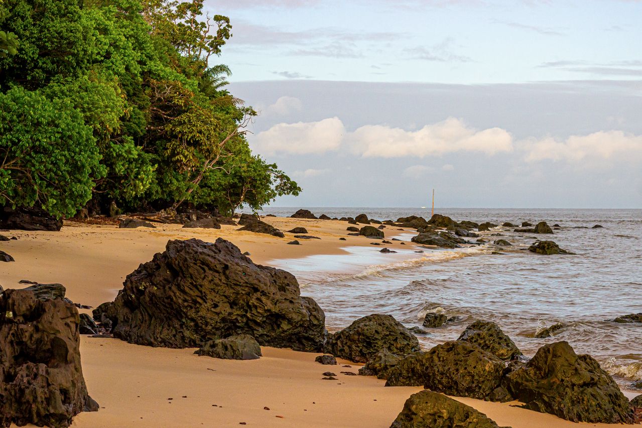 Best eSIM for French Guiana; a scenic coastal landscape with sandy beach, dark volcanic rocks, and turquoise water in French Guiana.