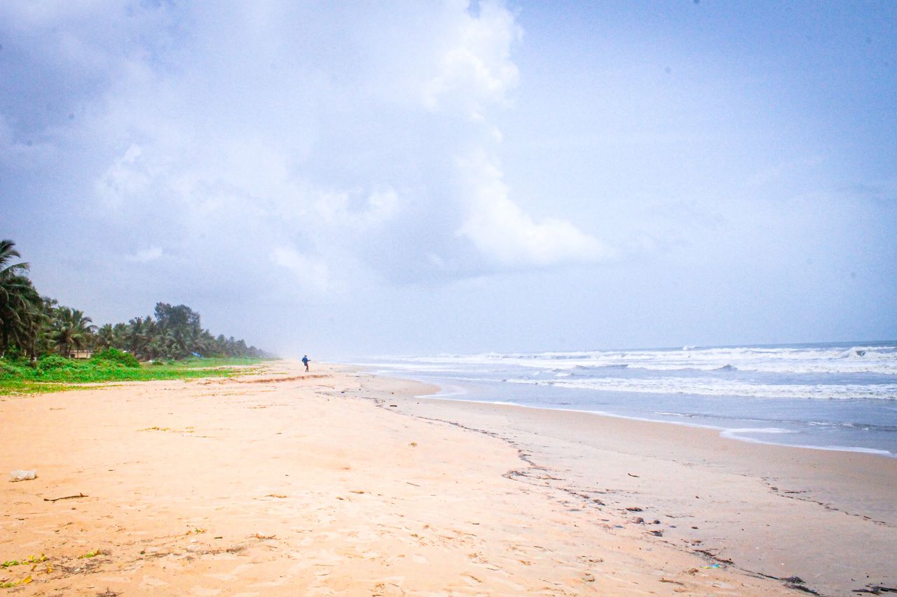 Best Ghana eSIM for travel; a wide sandy beach under a cloudy blue sky in Ghana, with the ocean waves on the right and green palm trees along the left side.