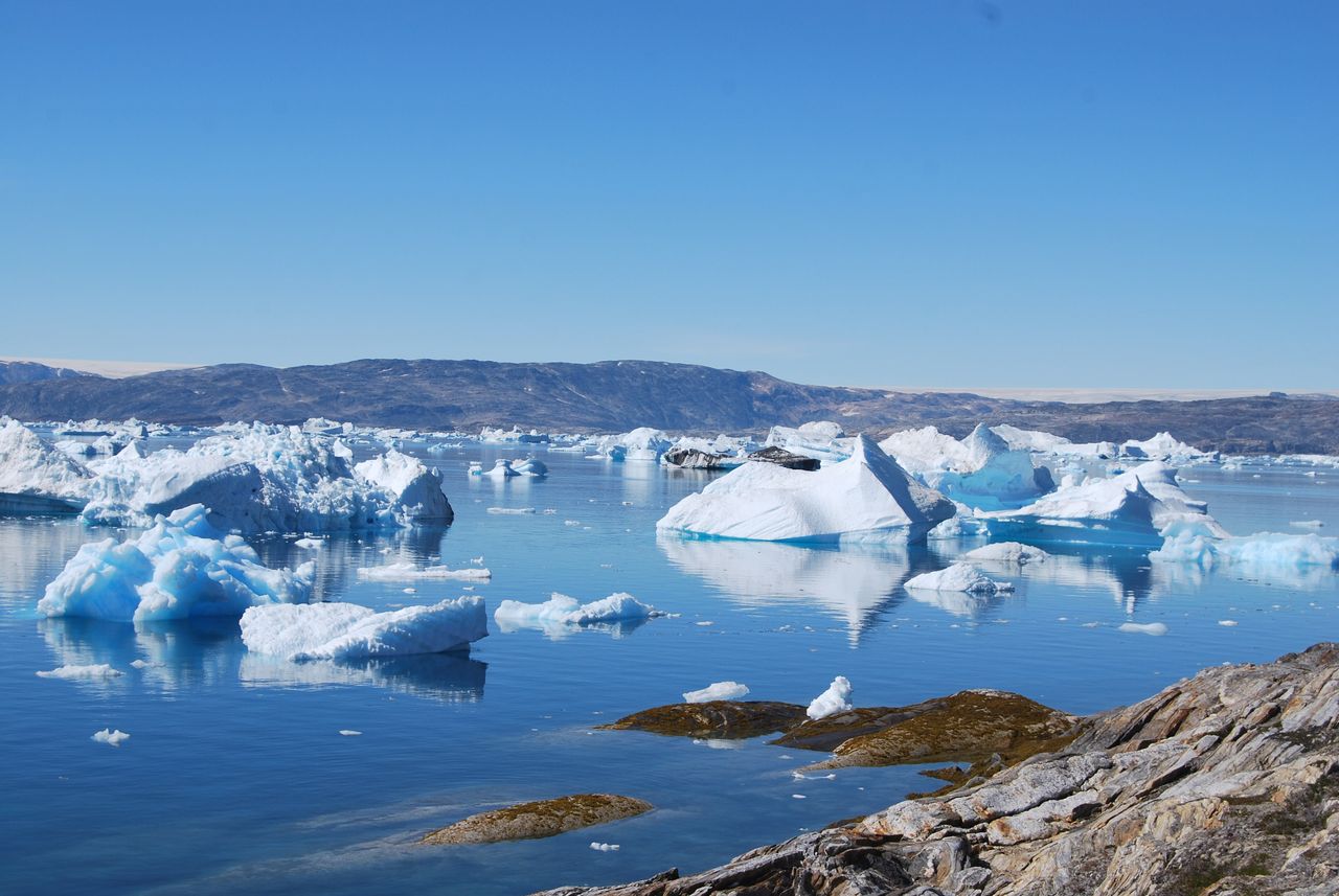Best eSIM for Greenland; a scenic landscape of a glacial lagoon in Greenland with floating icebergs in clear blue water under a bright blue sky.