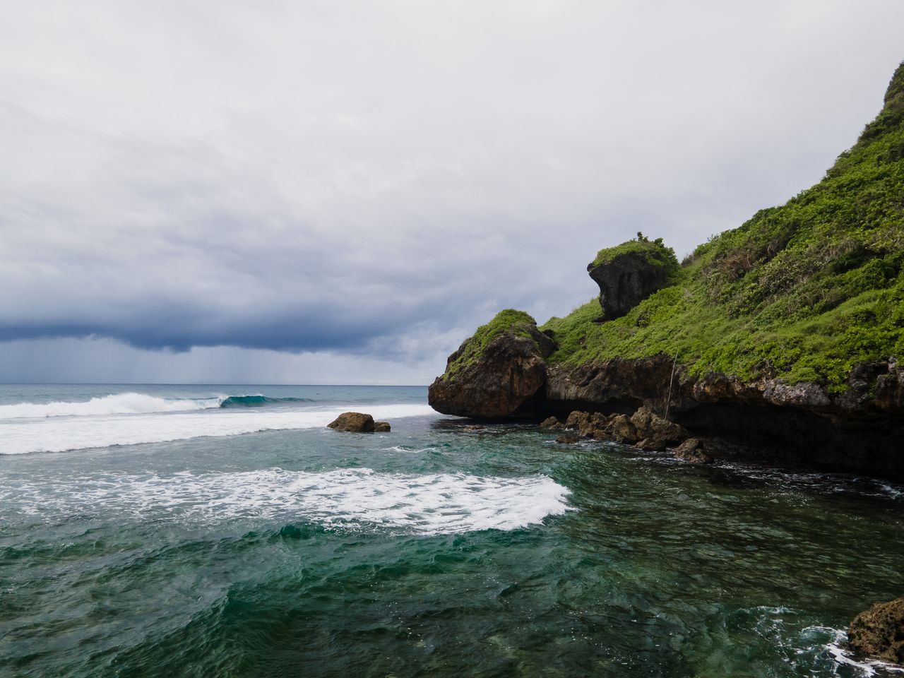 Best eSIM for Guam; a scenic shoreline with white foam waves and a lush green hillside in Guam.