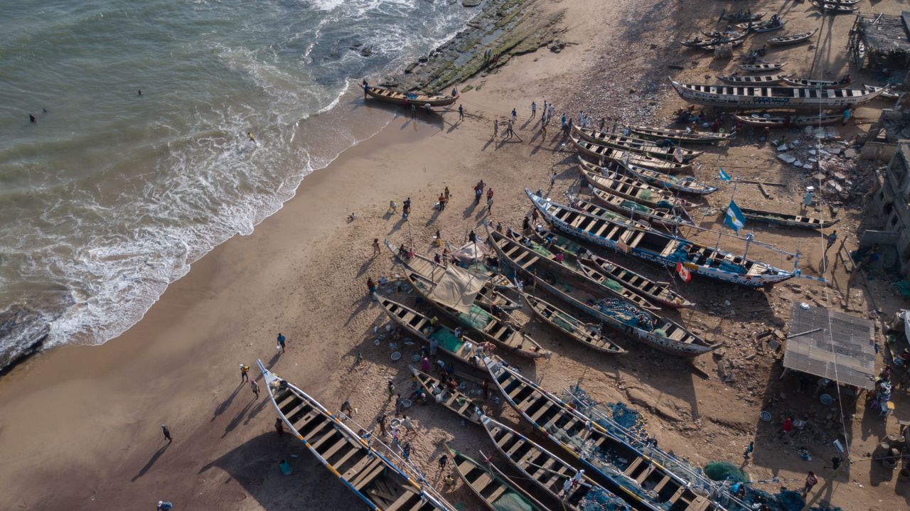 Best Guinea-Bissau eSIM for travel; a sandy beach with numerous traditional wooden boats docked on the shore, with waves crashing along the left side.