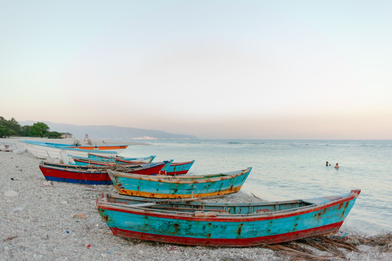 Best eSIM for Haiti; a beach scene showing traditional wooden boats beached along the shore with blue ocean on the right.