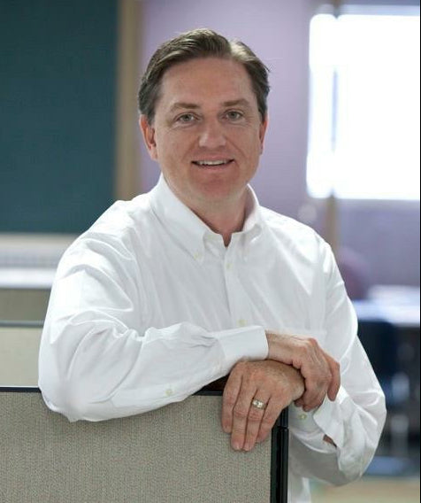 About Always Mobile: Our Founder in a white long-sleeve button-down shirt leaning on a cubicle divider in an office setting.