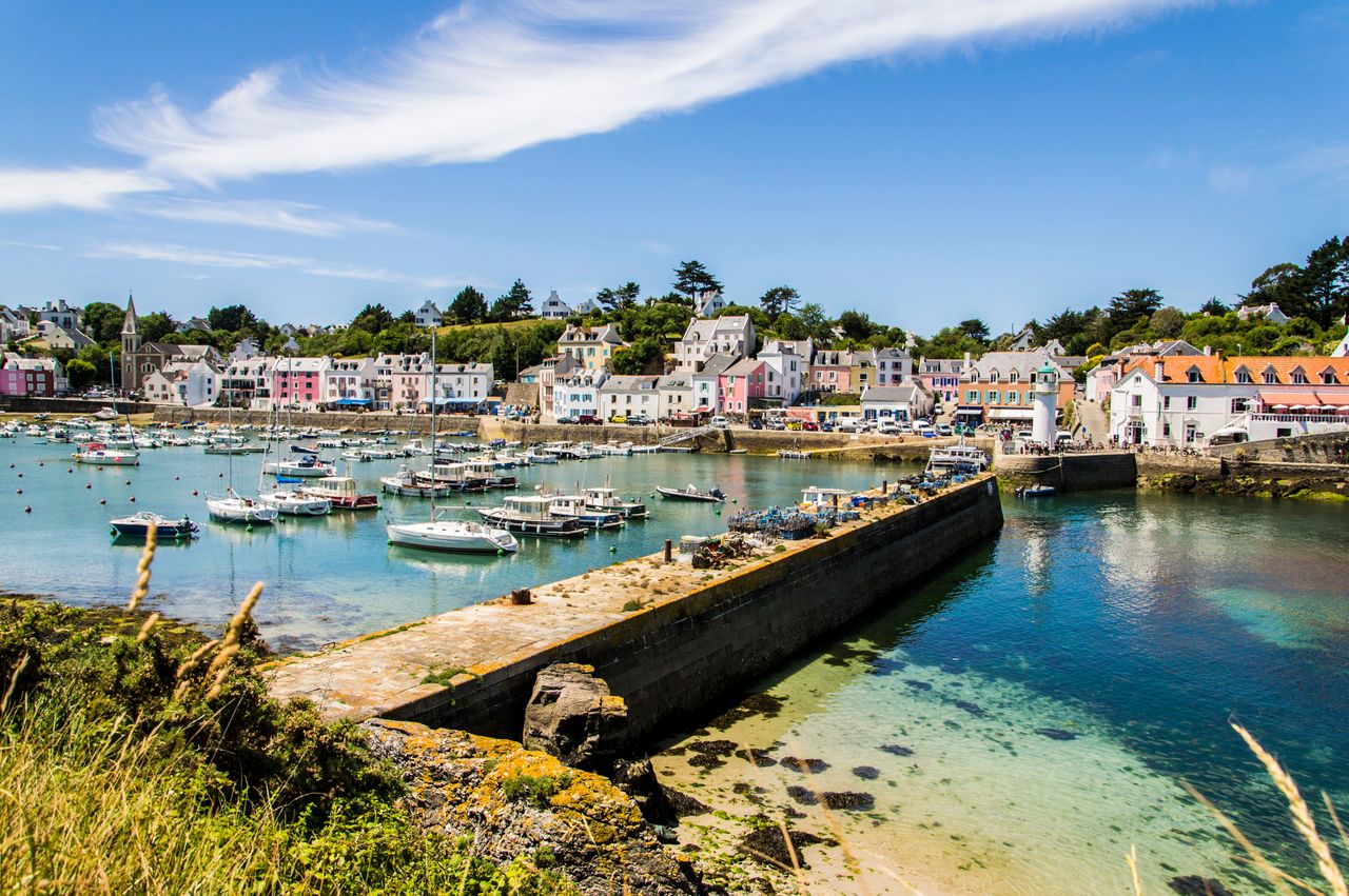 Best Jersey eSIM for travel; a scenic coastal harbor in Jersey with clear turquoise water, a stone breakwater, small boats anchored in the bay, and a row of colorful buildings on a hillside.