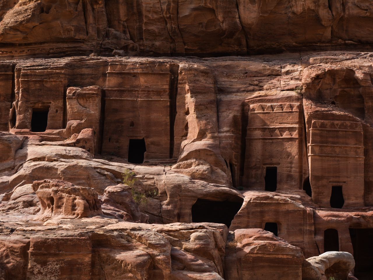 Best eSIM for Jordan; rock face with carved cave-like openings in Jordan and layered red sandstone formations in a desert canyon setting.