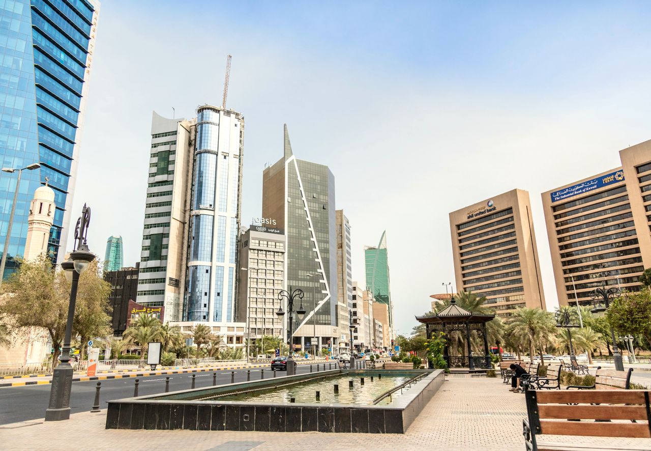 Best eSIM for Kuwait; a wide outdoor city plaza in Kuwait with a long rectangular fountain in the foreground, surrounded by modern high-rise office buildings.