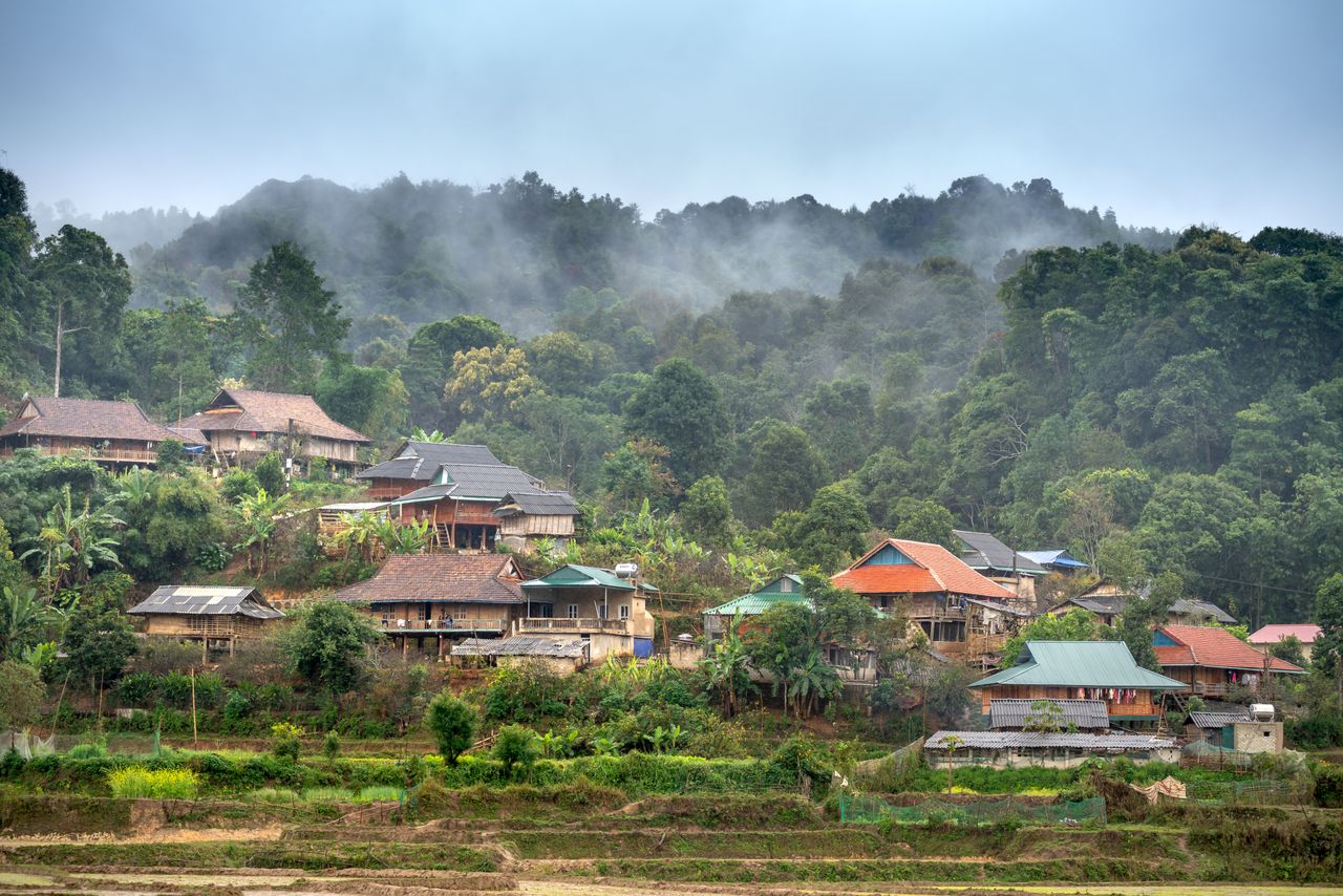 Best eSIM for Laos; a misty mountain village in Laos with clustered houses, terraced fields in the foreground, and dense green forest covering the hills.