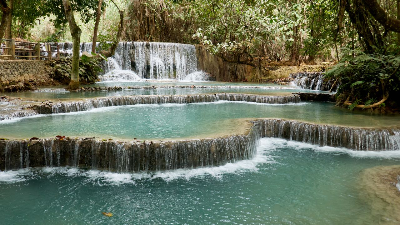 Best Laos eSIM for travel; a natural waterfall in Laos with multiple tiered pools of turquoise water, surrounded by dense green trees and foliage.
