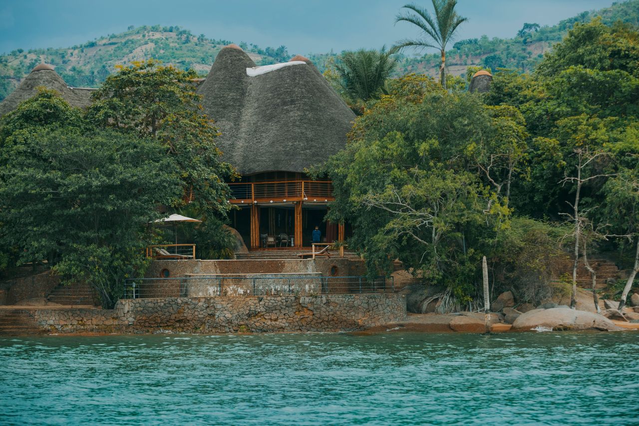 Best Malawi eSIM for travel; a tropical resort-style thatched-roof building situated on a rocky shoreline with calm blue water in the foreground.