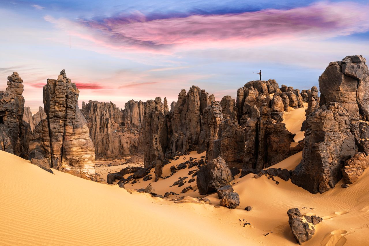 Best Mali eSIM for travel; a dramatic desert landscape in Mali with tall rock spires and sand dunes under a pastel sky with pink, purple, and blue clouds. 