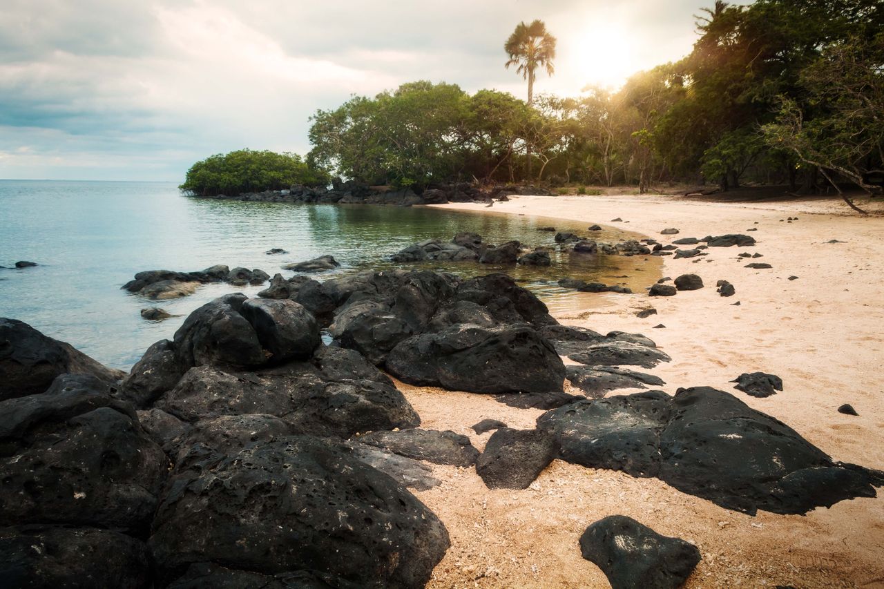 Best eSIM for Mayotte; rocky beach scene in Mayotte with black rocks in the foreground along a sandy beach.