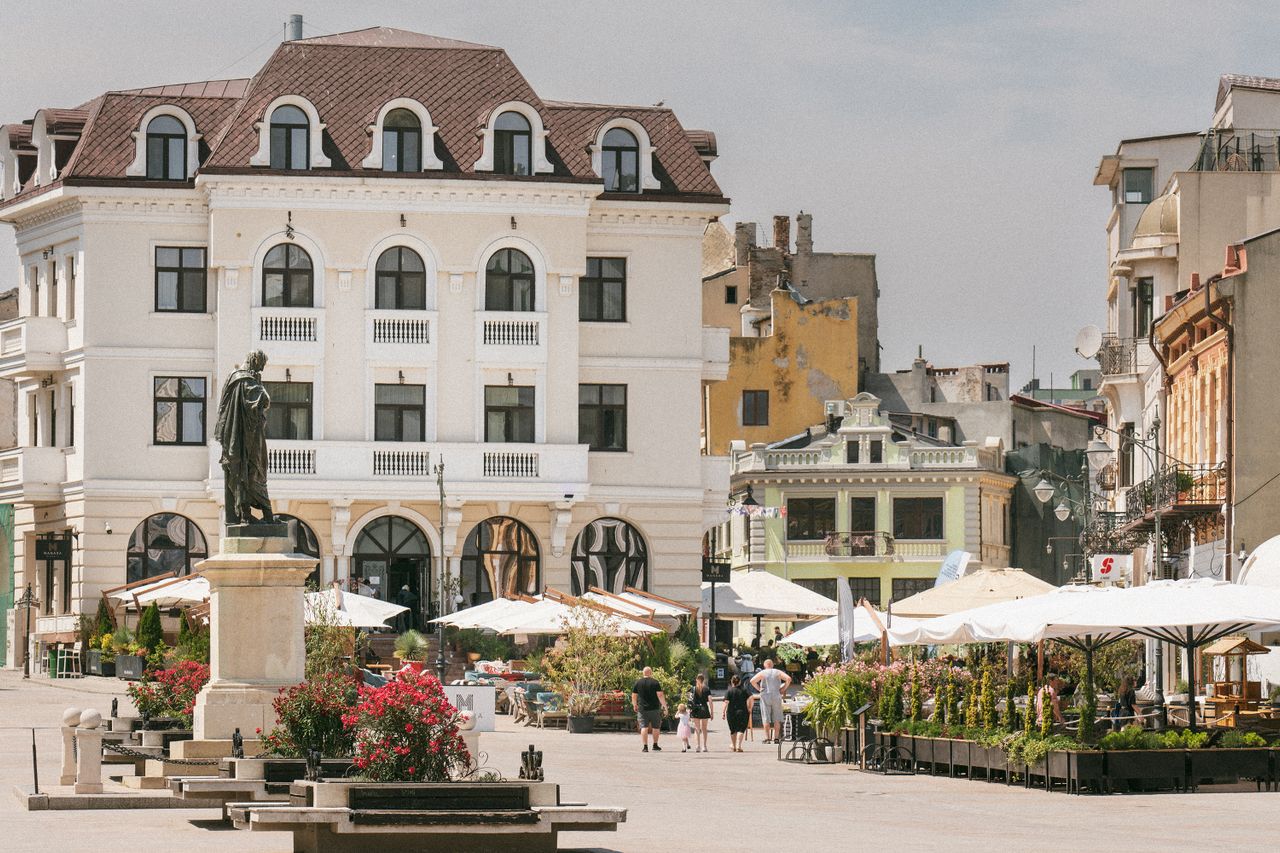 Best eSIM for Moldova travel; a photo of town square in Moldova with a large white building featuring a statue in front, outdoor cafe seating under white umbrellas.