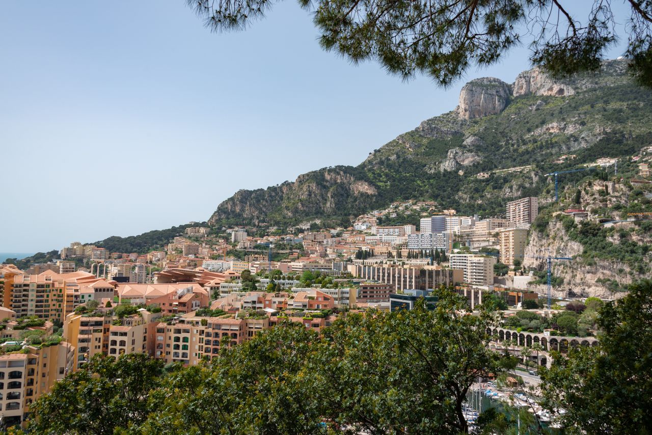 Best Monaco eSIM for travel; a scenic view of Monte Carlo city built into a steep green mountain, with buildings, roads, and rocky cliffs under a clear blue sky.