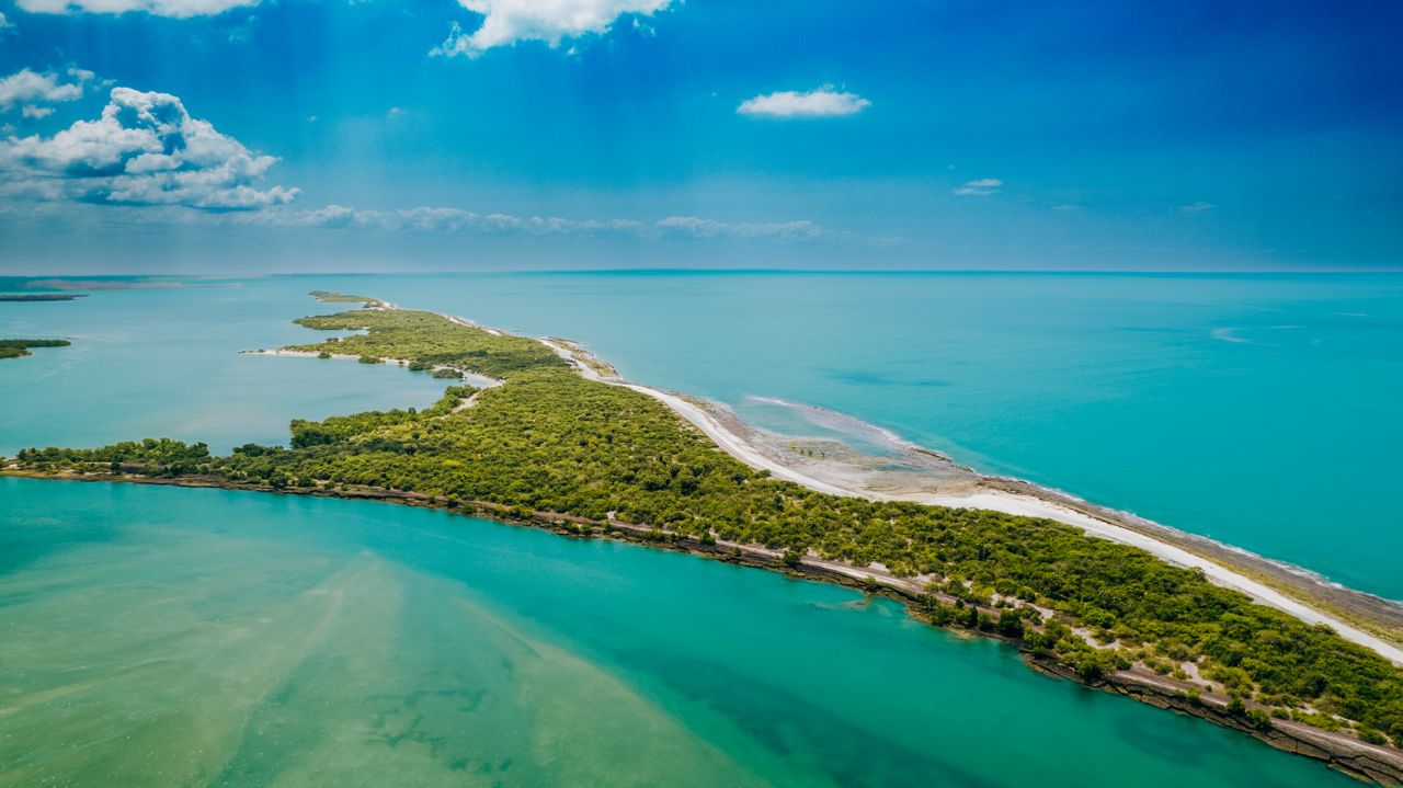 Best Mozambique eSIM for travel; aerial view of a narrow green sandbar in Mozambique stretching diagonally through bright turquoise and deep blue water.