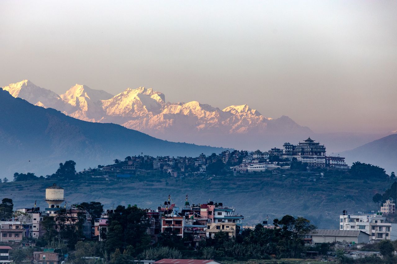 Best Nepal eSIM for travel; a Nepal cityscape with buildings and trees in the foreground, snow-capped mountains in the background. 