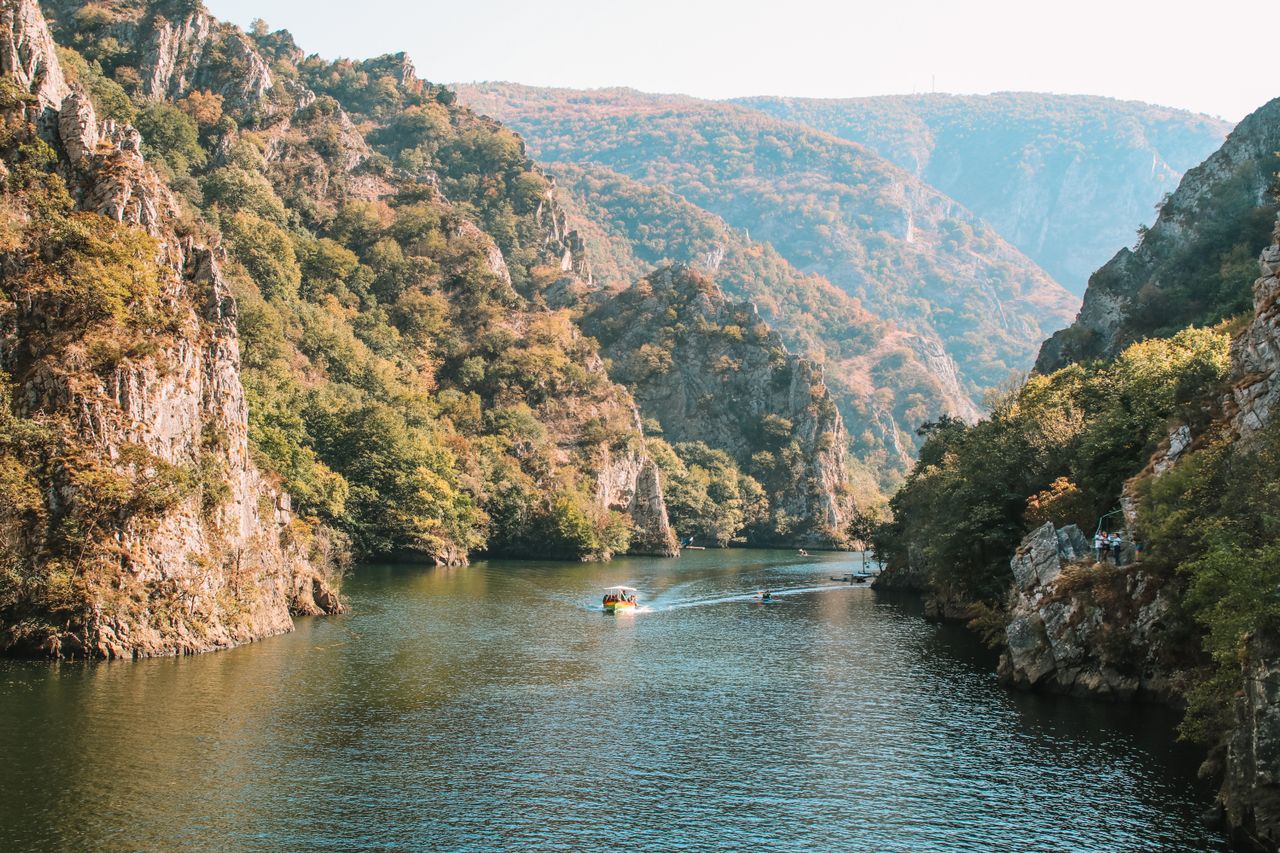 Best North Macedonia eSIM for travel; a scenic view of a deep canyon in North Macedonia with steep rocky cliffs covered in green and brown vegetation, a river flowing through the center.
