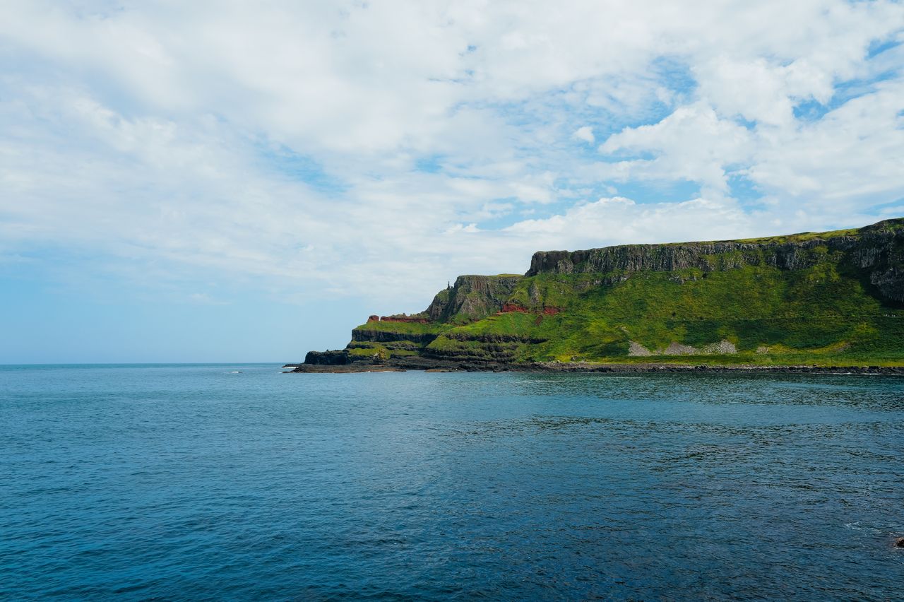 Best Northern Ireland eSIM for travel; a coastal landscape in Northern Ireland with deep blue ocean water in the foreground, a grassy green cliffside on the right.