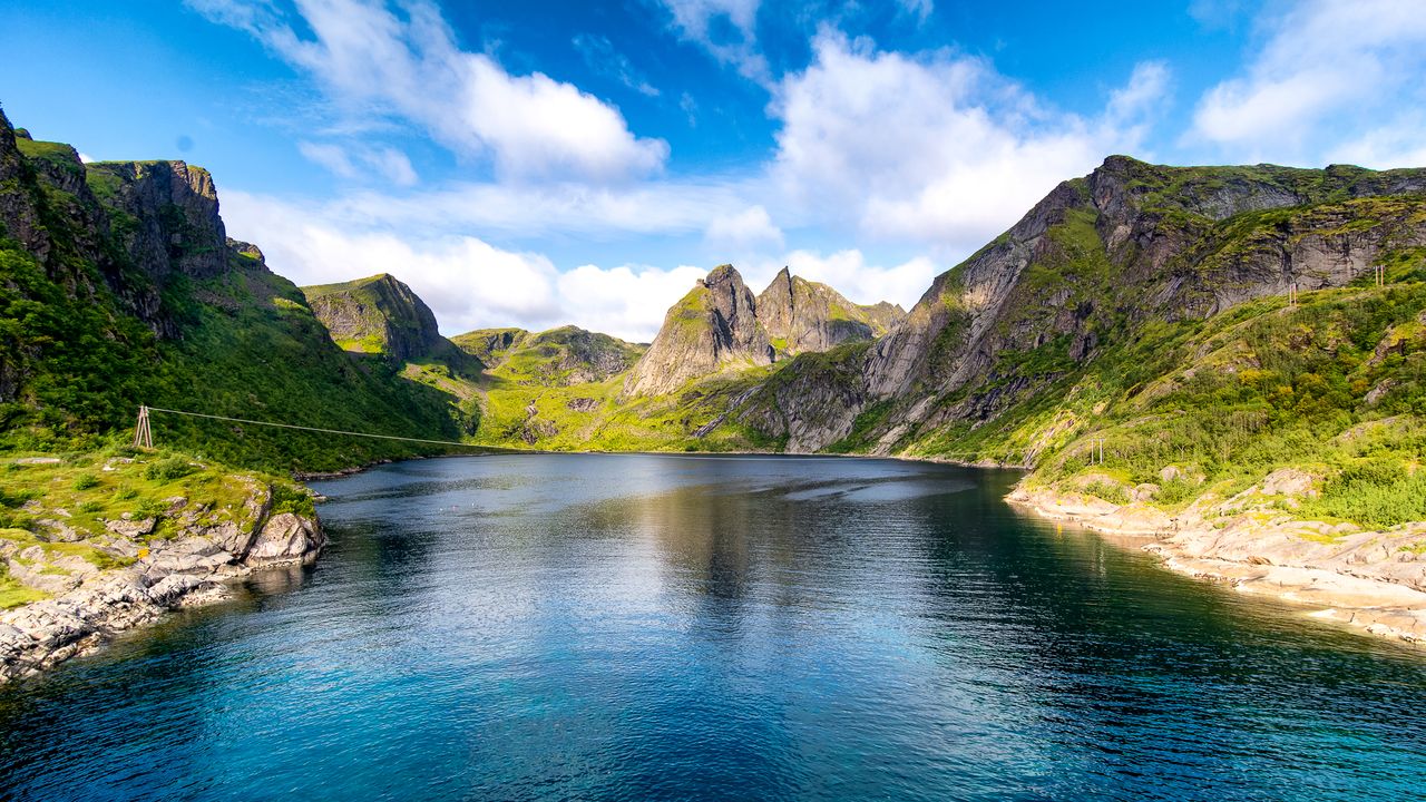 Best eSIM for Norway - photo of a scenic landscape with a deep blue fjord winding between steep green mountains under a bright blue sky in Norway