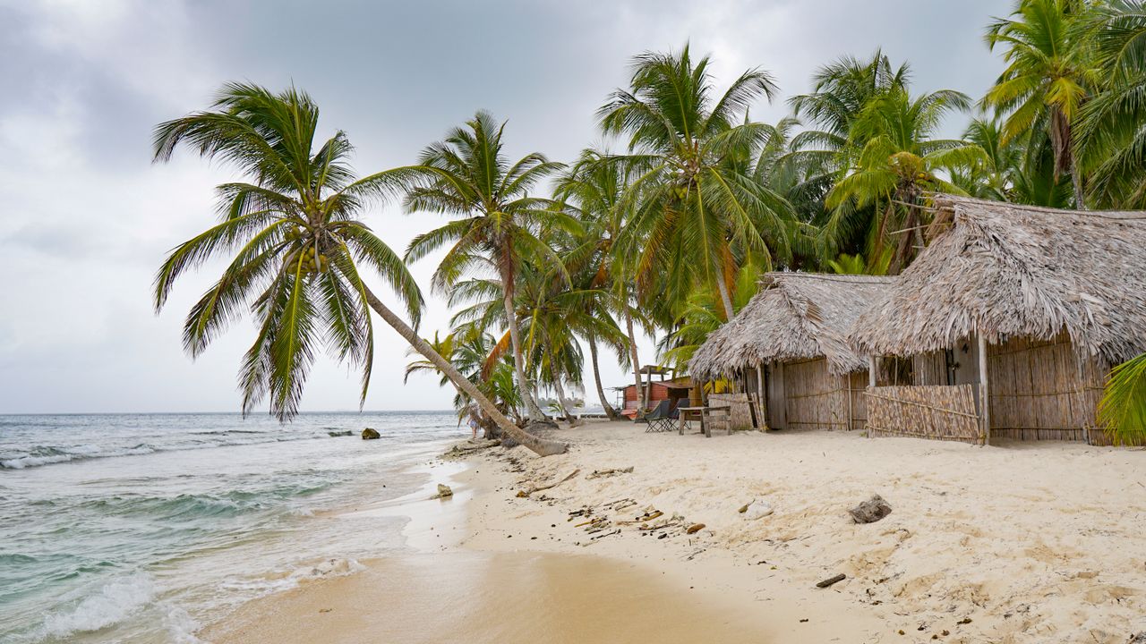 Best eSIM for Panama travel; a beach scene with thatched huts and palm trees on a cloudy day in Panama.