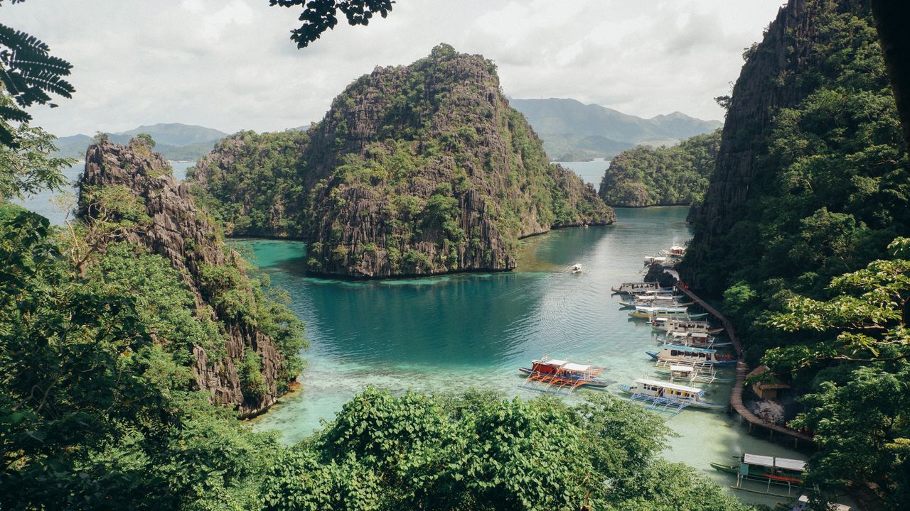 Best Philippines eSIM for travel; a tropical bay in the Philippines with steep green karst islands rising from turquoise water, with small boats anchored along a shoreline.
