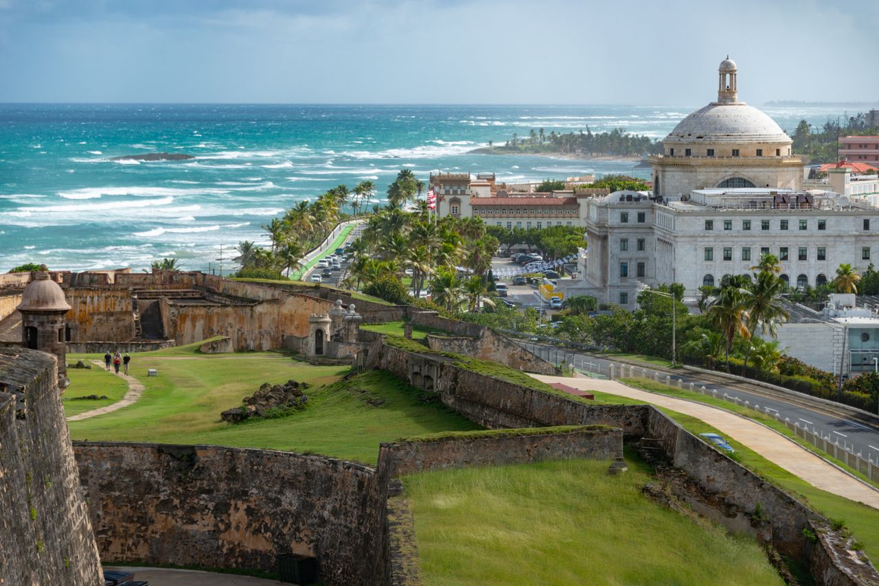 Best eSIM for Puerto Rico travel; a scenic coastal view in Puerto Rico featuring historic stone fort walls with green grass, a large white domed building.