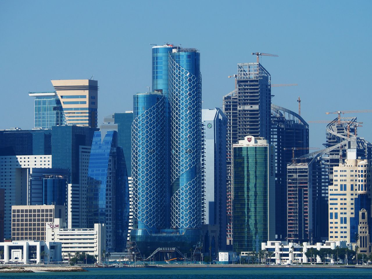 Best Qatar eSIM for travel; Doha, Qatar skyline with several modern blue glass skyscrapers, including two prominent curved towers in the center, under a clear blue sky.