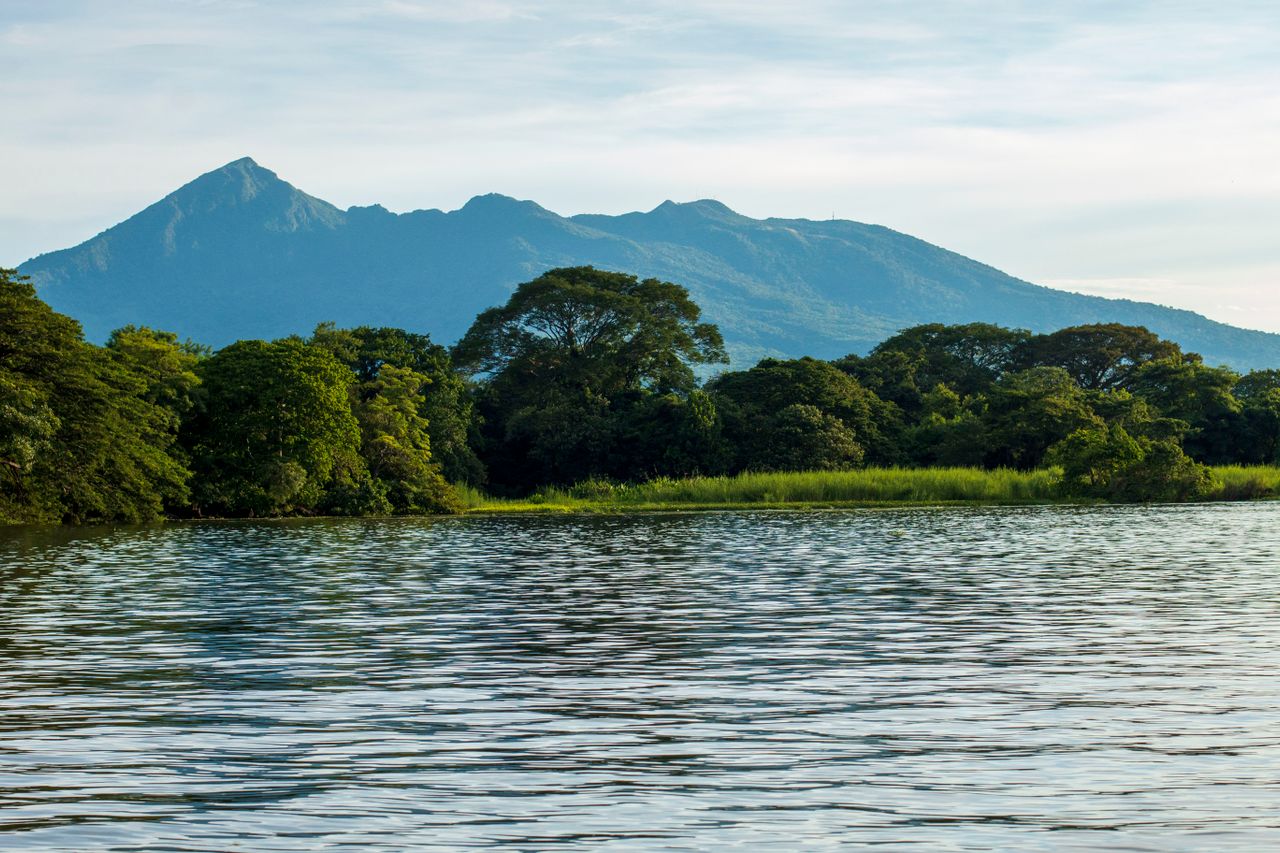 Best Republic of the Congo eSIM for travel; a calm body of water in the foreground, a line of green trees, and a large blue mountain in the background in the Congo.