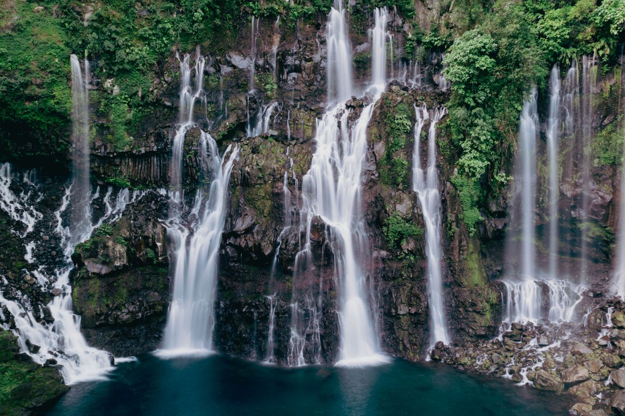 Best Reunion eSIM for travel; a scenic view of a multi-tiered waterfall on Reunion Island cascading down a dark rocky cliff.
