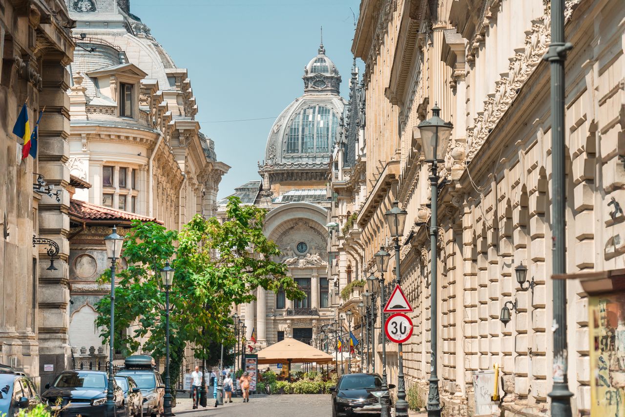 Best eSIM for Romania - photo of sunny street view in Romania with ornate beige stone buildings, a domed cathedral in the background.