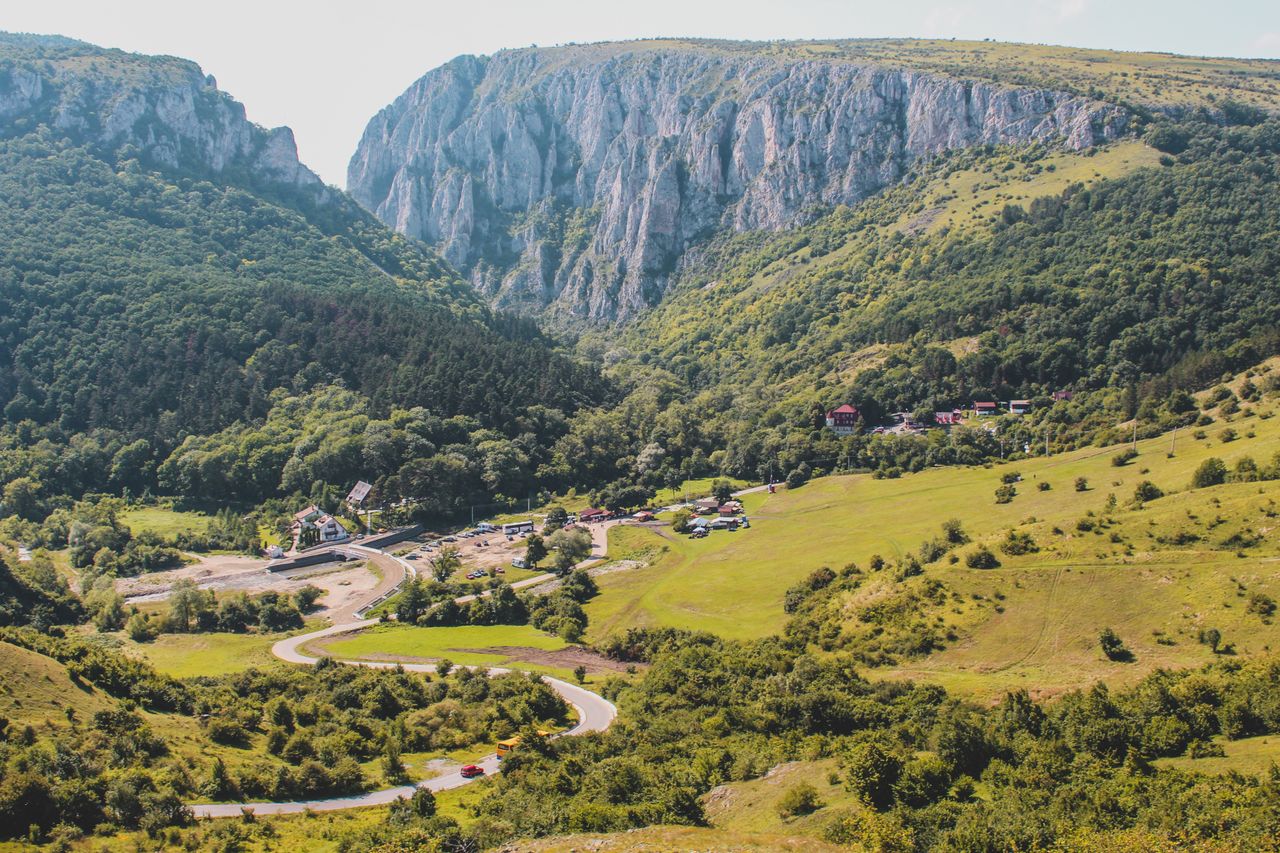 Best Romania eSIM for travel - photo of a scenic aerial view of a deep mountain valley with steep rocky cliffs, dense green forests, rolling grassy hills in Romania.
